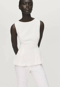 Top peplum bianco con scollatura rotonda, caratterizzato da pieghe strutturate e una texture liscia, abbinato a pantaloni bianchi aderenti.