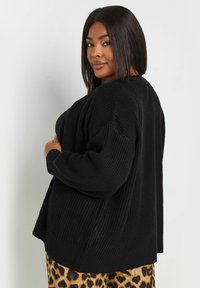 Svart, texturerad stickad cardigan med en lös passform, vida ärmar och en sidofransk, kombinerad med leopardmönstrade byxor.