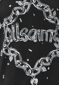 Grafica di catena bianca con collegamenti a forma di cuore e testo "AllSaints" su tessuto nero, decorata con piccoli strass trasparenti sparsi.