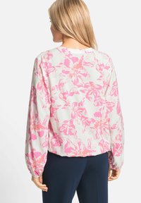 Blouse florale en tissu léger avec un motif de fleurs roses. Présente des manches longues avec des poignets froncés et un col rond. Vue de dos montrée.