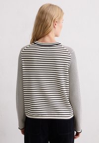 Gestreifter Pullover mit schwarz-weißen horizontalen Streifen, gestrickter Textur, runden Ausschnitt und langen Ärmeln, kombiniert mit dunklen Hosen.