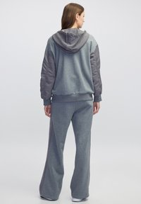 Sudadera gris con un panel en gris más oscuro que contrasta, combinada con pantalones de chándal de pierna ancha a juego. La tela parece suave y tiene un corte relajado.