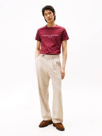 Bordový bavlnený tričko s potlačou "TOMMY HILFIGER EST. 1985", spárované so svetlými béžovými nohavicami a hnedými semišovými mokasínami.