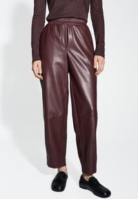 Pantaloni in pelle bordeaux con cintura elastica, vestibilità comoda e texture liscia. Abbinati a calzature nere per un contrasto.