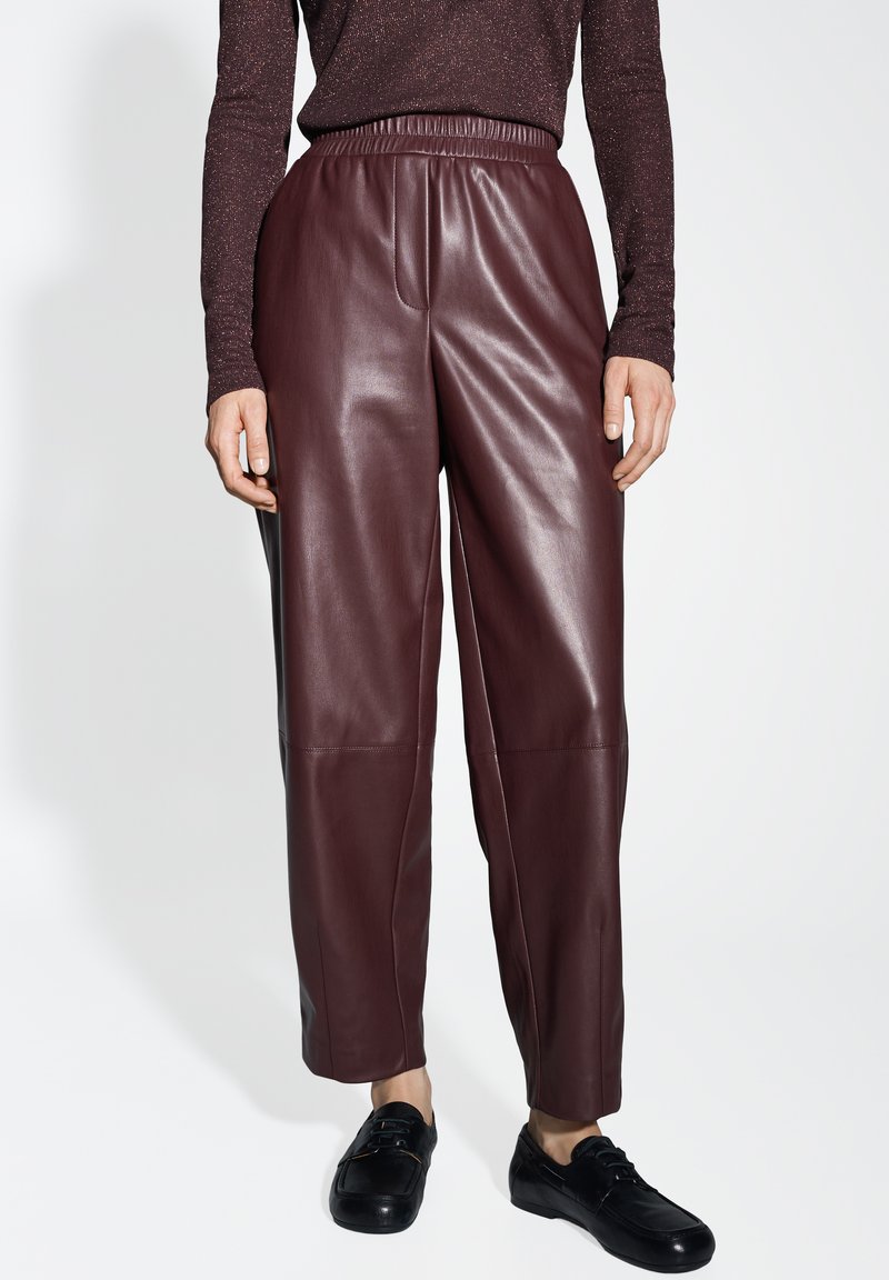 Pantaloni in pelle bordeaux con cintura elastica, vestibilità comoda e texture liscia. Abbinati a calzature nere per un contrasto.