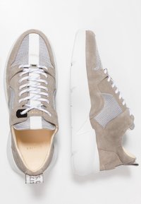 Jasnoszare sportowe trampki zamszową cholewką, siateczkowymi akcentami, białymi sznurowadłami i grubą białą podeszwą, z oznaczeniem marki na tylnej części.