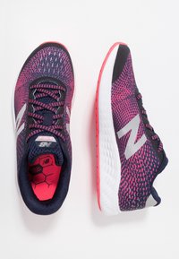 Běžecké boty s prodyšným vrškem z navy modré síťoviny s růžovými akcenty, černými tkaničkami a bílou mezipodešví s růžovou podrážkou. Stříbrný detail loga.