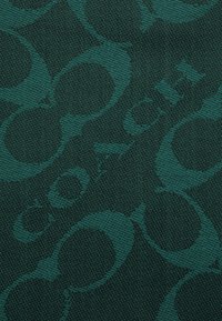 Tissu tissé vert présentant un motif répété de cercles entrelacés et le mot "COACH" affiché en évidence. Surface texturée.