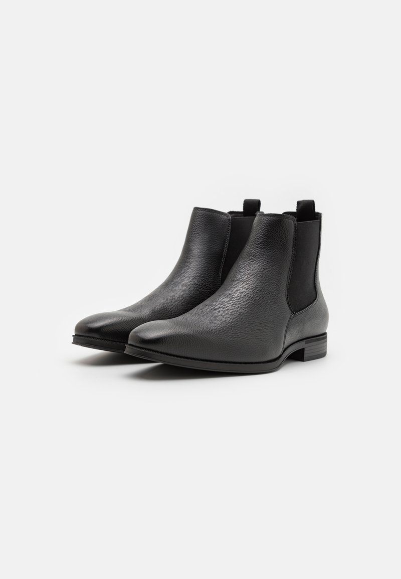 Bottines Chelsea en cuir noir avec un design épuré, bout rond, panneaux latéraux élastiques et petit talon. Finition texturée subtile.