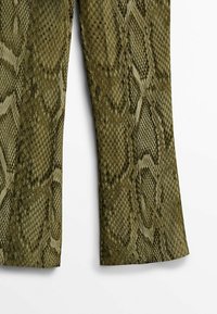 Pantalons verts à motif serpent avec un tissu texturé. Dotés d'un ourlet évasé et d'un design d'écailles, alliant surfaces lisses et surélevées.
