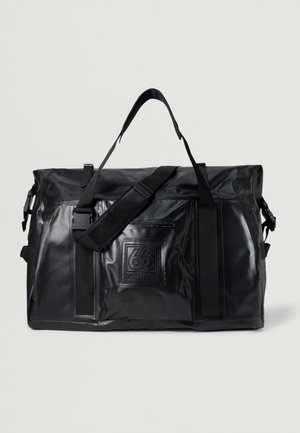 Bolsa de viaje negra, impermeable, con textura suave, correa de hombro ajustable, bolsillo lateral con cremallera y detalle de logo en relieve en la parte frontal.