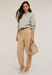 Felpa grigia con collo abbellito, pantaloni cargo beige, borsa beige con dettagli in metallo e scarpe con tacco nude.