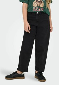 Černé džínové široké kalhoty s vysokým pasem, kontrastním prošíváním a klasickým pětiokovým designem, v kombinaci s černými teniskami.