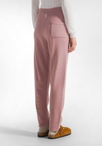 Rosa Lounge-Hosen aus weichem Stoff, mit einem elastischen Bund und einer Gesäßtasche, kombiniert mit braunen Schuhen.