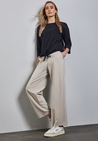 Suéter negro de corte holgado con mangas de tres cuartos, combinado con pantalones anchos beige que tienen un cinturón ajustable. Zapatillas blancas con detalles.