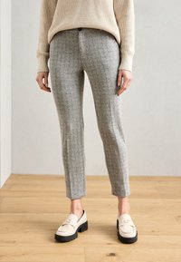 Grijs houndstooth-patroon broek met een slim fit, gecombineerd met crème loafers met een dikke zwarte zool. Achtergrond van natuurlijk houten vloer.