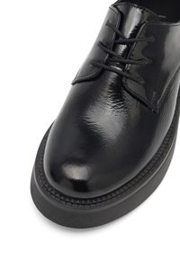 Pantof lung din piele lucioasă neagră, cu vârful rotunjit, având șireturi subțiri, talpă plată și cusături subtile de-a lungul marginii.