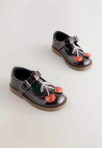 Patentierte dunkelviolette Lacklederschuhe mit einem silbernen Schnürsenkeldesign und roten Kirschakzenten, verstellbarem Riemen und brauner Gummisohle.