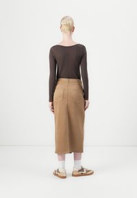 Braunes langärmliges Oberteil mit Rundhalsausschnitt, kombiniert mit einem beige, knielangen Rock mit aufgesetzten Taschen hinten, getragen mit weißen Socken und gemusterten Sneakers.