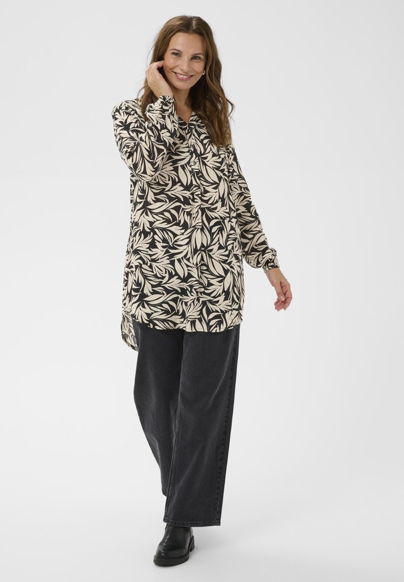 Chemise à manches longues noire et crème avec imprimé feuillage, dotée d'un devant boutonné et d'un ourlet arrondi, associée à un pantalon noir à jambes larges.