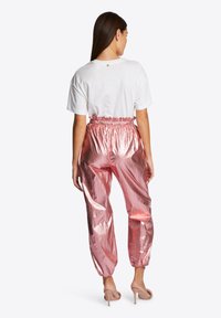 Rosa metallische Jogginghosen mit elastischem Bund und gerafften Knöcheln, kombiniert mit einem weißen T-Shirt. Glatte, glänzende Textur, lässige Passform.