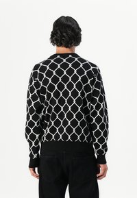 Sort striktrøje med et diamantmønster i hvidt. Ribbet manchetter og kant. Casual design, vist fra ryggen, der afslører det mønstrede stof.