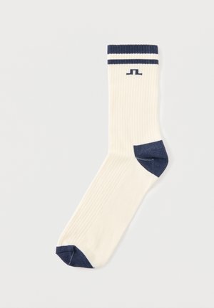 Chaussette côtelée couleur crème avec talon, pointe, bordure bleu marine et deux rayures près du haut, présentée à plat sur un fond blanc.