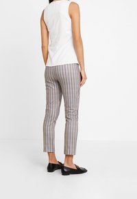 Top bianco senza maniche con dettagli cuciti, abbinato a pantaloni attillati a scacchi nei toni del navy, beige e marrone. Scarpe flat nere.