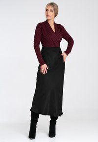 Bordowa bluzka z długim rękawem w stylu kopertowym w białe kropki, zestawiona z elegancką, czarną satynową spódnicą maxi i czarnymi, wysokimi butami do kolan.