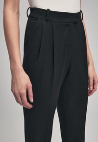 Zwarte op maat gemaakte broek met een hoge taille, voorzien van plooien en riemlussen. Gemaakt van gladde stof, met een schone, gestructureerde uitstraling.