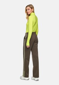 Long-sleeve neon green top paired with brown joggers featuring white and neon yellow side stripes; model stands sideways with a relaxed fit.