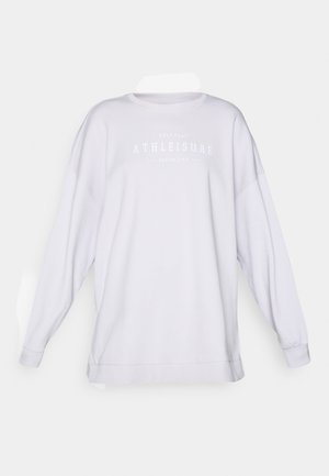 Bijela oversized dukserica s dugim rukavima, okruglim izrezom i ispisanim tekstom "ATHLEISURE" u suptilnoj sivoj boji preko grudi. Mekana tkanina.
