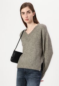 Grå ullgenser med v-hals, ribbet kant og sideåpninger, kombinert med mørk denimjeans og en liten svart skulderveske.