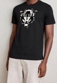 Černé bavlněné tričko s grafickým motivem stylizované tygří hlavy v bílé barvě. Krátké rukávy s kulatým výstřihem, hladká textura.