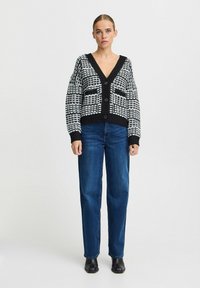 Melnas un baltas rakstainas kardigānas ar dziļu V-veida kakla izgriezumu, pogu aizdari un ribotiem piedurkņu galiem, kombinēts ar ziliem taisnajiem džinsiem un melnām zābakiem.