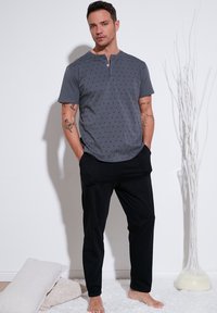 Camisa henley de manga corta gris con un patrón sutil, combinada con pantalones negros de corte holgado. Textura suave, diseño informal y sin accesorios visibles.