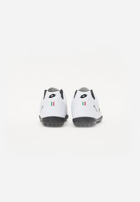 Baskets blanches avec une semelle en caoutchouc noir, arborant un design élégant, un talon arrondi et un petit accent de drapeau italien à l'arrière.