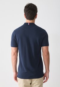 Navyblauwe polo shirt gemaakt van katoen, met korte mouwen en een kraag met een rood-witte accent achter op de nek. Gladde textuur.