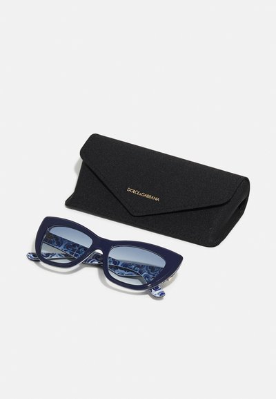 Navy cat-eye sunglasses with gradient lenses, intricate patterned temple accents, and a black textured case featuring a gold logo.