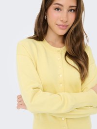 Gele gebreide cardigan met ronde halslijn, lange mouwen en centrale knoopsluiting. Gladde textuur en aansluitend ontwerp.