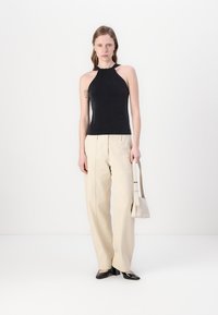 Crna halter majica s prilagođenim dizajnom, uparena s kremastim širokim hlačama. Model drži malu bijelu torbicu.