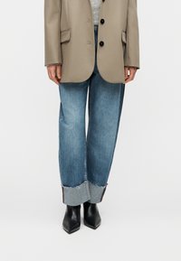 Φωτεινό μ πεζ σακάκι με μαύρα κουμπιά, σε συνδυασμό με άνετα μπλε τζιν παντελόνια με ξέφτια στο τελείωμα και ανοιχτόχρωμη μανσέτα από ντένιμ. Μαύρα μυτερά μποτάκια.