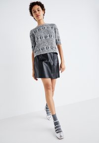 Pull en mailles épaisses gris avec des manches courtes, associé à une jupe noire en simili cuir. Le modèle porte des chaussures argentées et des chaussettes grises.