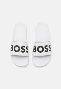 Valkoiset liukumäen sandaalit, joissa on teksturoitu hihna, jossa on rohkeaa mustaa "BOSS" -kirjoitusta, sileä pohja ja minimalistinen muotoilu.