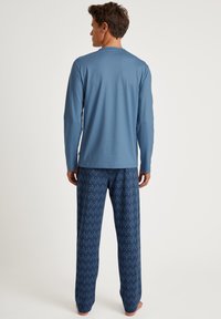 Haut à manches longues bleu associé à un pantalon de pyjama marine à motifs présentant un design géométrique répétitif. Tissu doux et léger.
