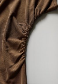 Brauner geripptes Material mit gerafften Details entlang der Kante, das eine weiche Textur und fließende Form zeigt. Ideal für Freizeit- oder Sportbekleidung.