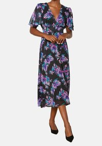 Svart blommig klänning med lila och turkosa mönster, med korta volangärmar och v-ringning, som faller till mitten av vadbenet. Bärs med svarta klackskor.