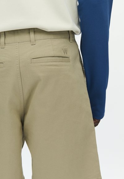 Shorts beige à texture lisse avec deux poches arrière et un logo brodé en "W". Associés à une chemise bleue à manches longues.