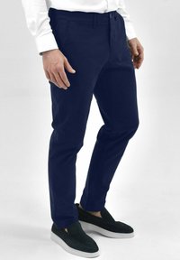 Navyblauwe broek van lichtgewicht stof, met een slim fit ontwerp, vooraan pockets en een knoopsluiting. Gecombineerd met zwarte instappers.