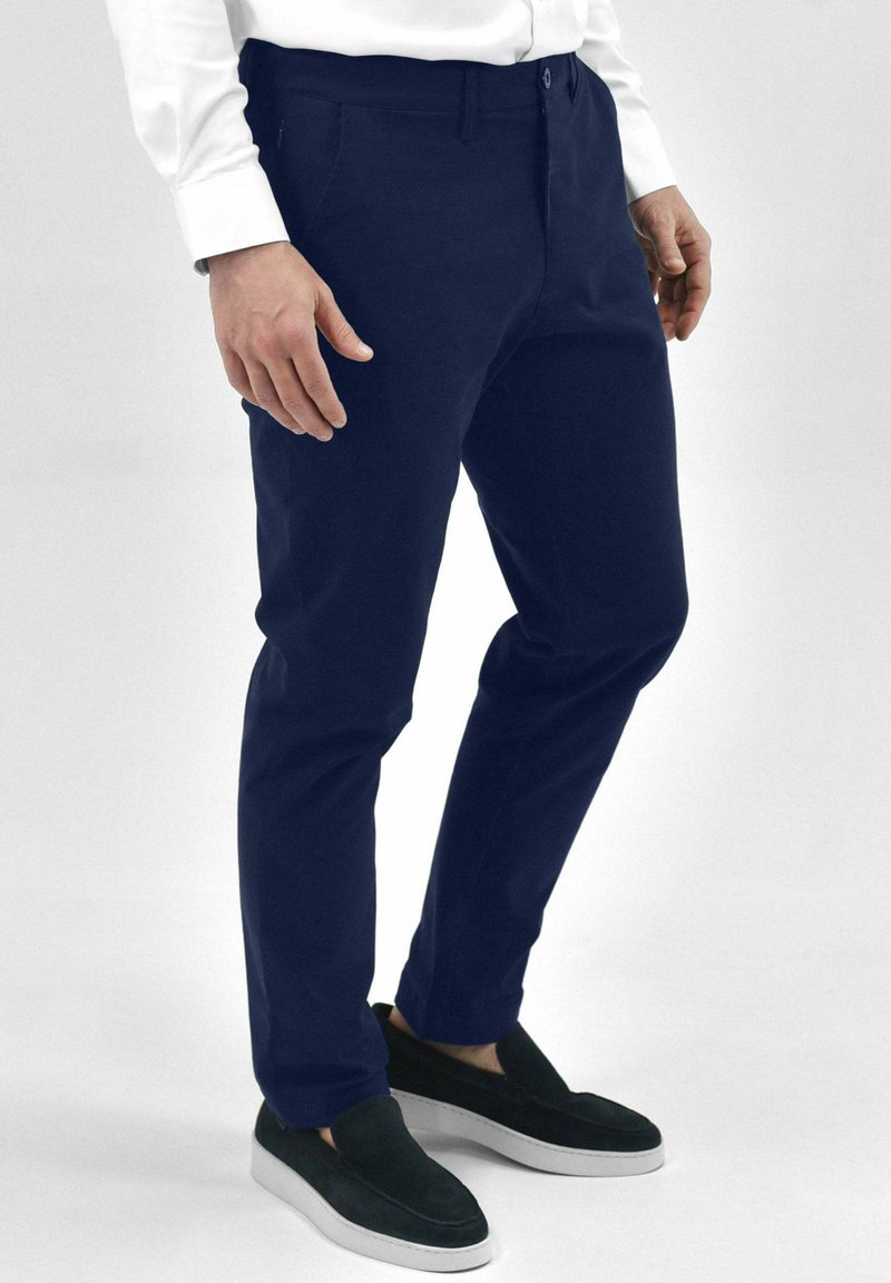 Navyblauwe broek van lichtgewicht stof, met een slim fit ontwerp, vooraan pockets en een knoopsluiting. Gecombineerd met zwarte instappers.